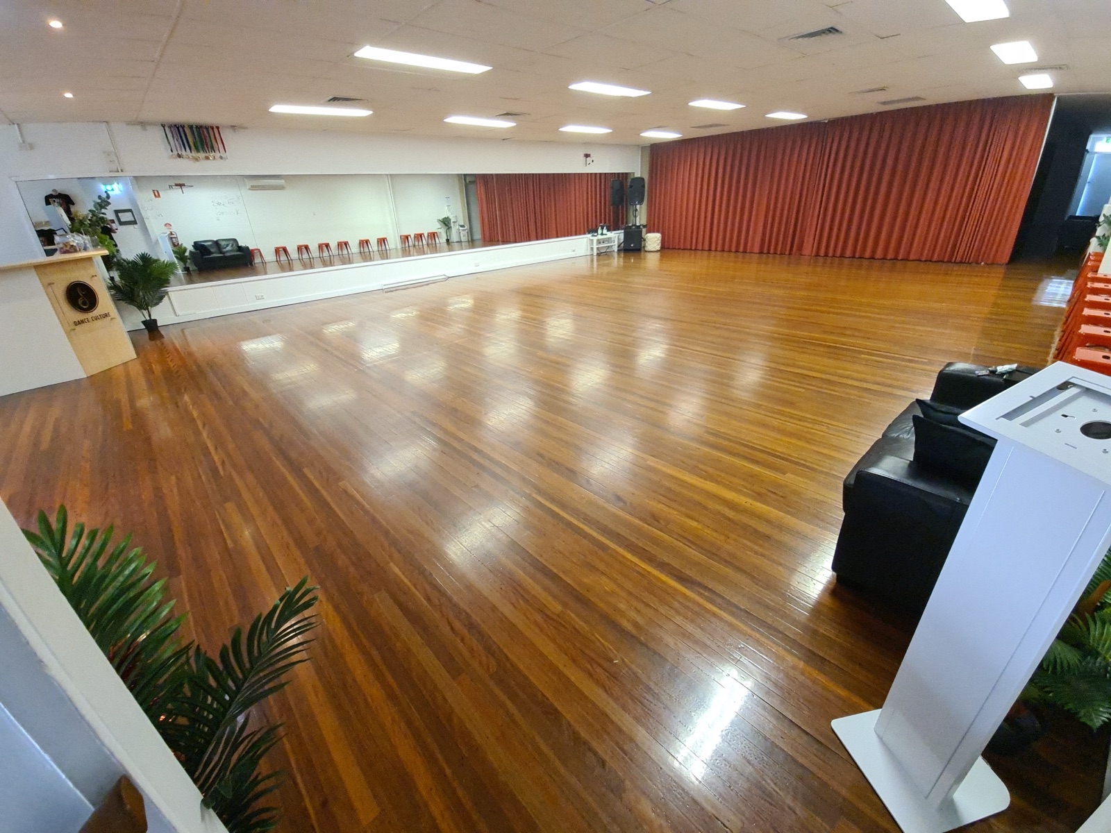 Studio 1 at Dance Culture Annerley: a large polished hardwood dance floor with full-length mirrors and red stage curtains