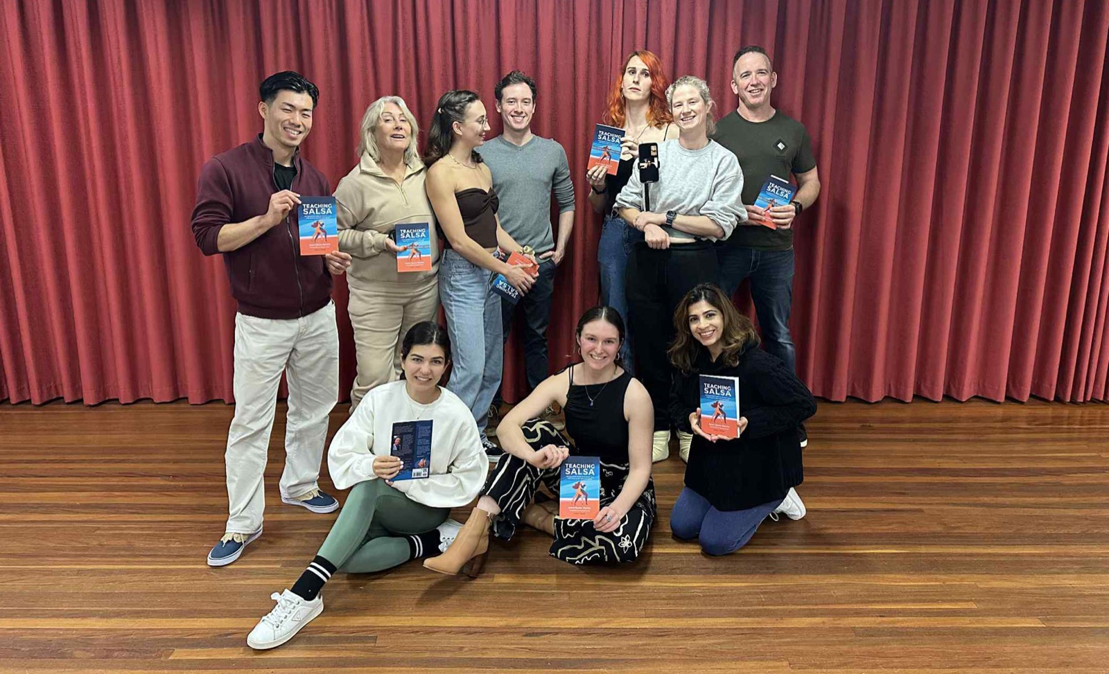 A Dance Culture instructor training cohort holding their copies of Teaching Salsa